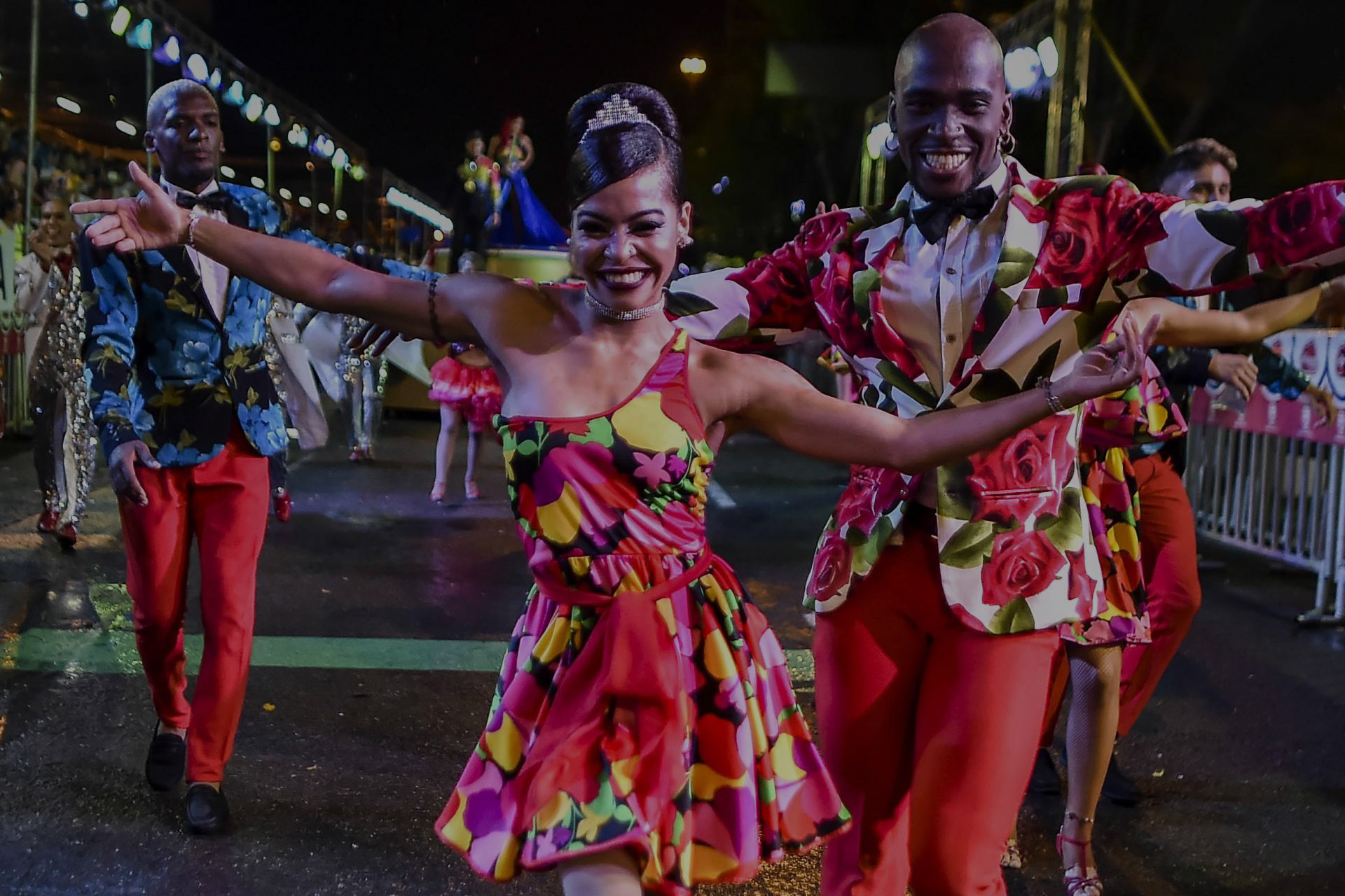 Pareja de bailarines con vestimenta roja y detalles florales bailando en medio de la calle.