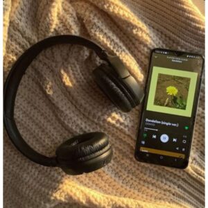 Un celular con una canción en Spotify reproduciéndose y unos audífonos de diadema.