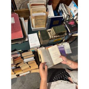 Una persona leyendo un libro y al fondo cientos de libros apilados en distintas posiciones y columnas.